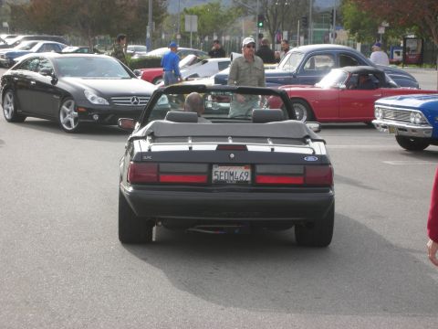 1998 Ford Crown Victoria - rear of a black Fox-body Ford Mustang convertible with California plate, moving through a car show crowd.