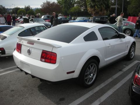 1998 Ford Crown Victoria - white Ford Mustang Shelby GT coupe with rear spoiler and silver wheels parked at a busy outdoor car show.