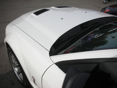 1998 Ford Crown Victoria - Close-up of a white Ford Mustang's hood with louvered vents and windshield, with reflections in the dark glass.
