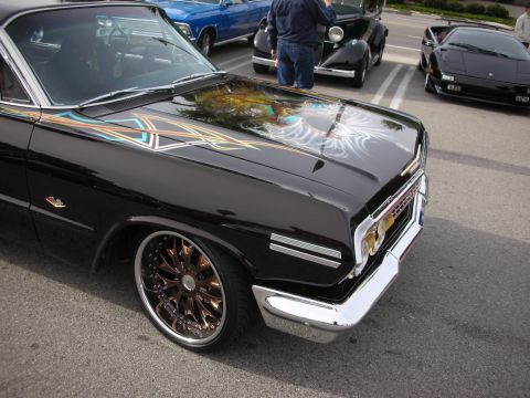 1998 Ford Crown Victoria - lowered black mid-1960s Chevrolet Impala with an airbrushed hood mural and wire-spoke wheels at a car show.