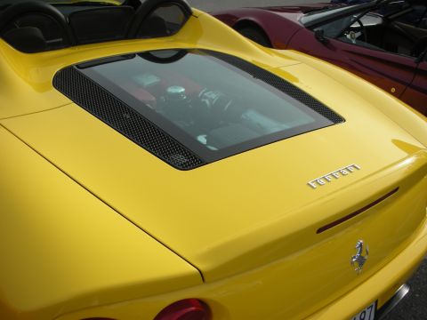 1998 Ford Crown Victoria - Close-up of a yellow Ferrari's rear engine cover, glass window and chrome prancing-horse emblem, with a maroon sports car behind it.