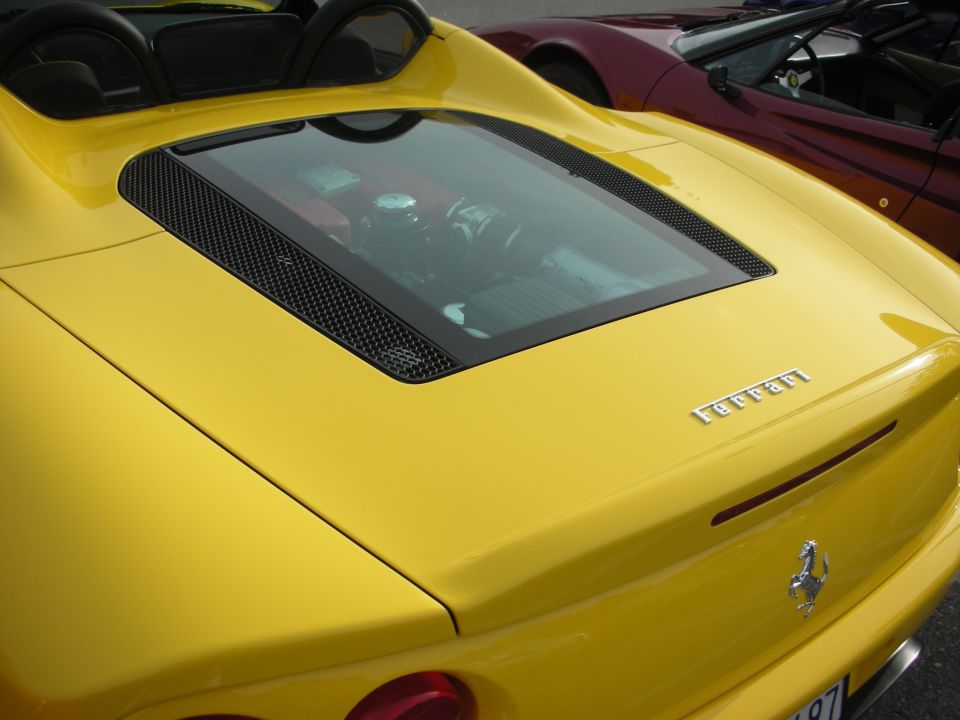 Rear deck of a yellow Ferrari convertible with mesh engine cover and prancing-horse badge