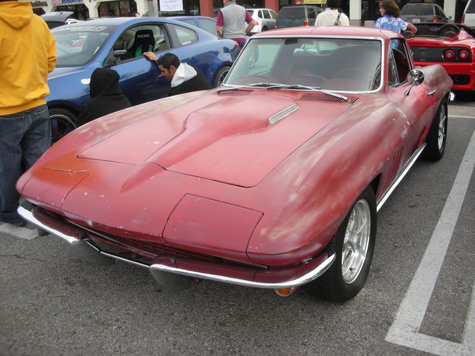 Front of a faded red Chevrolet Corvette fastback with chrome bumpers at a car show