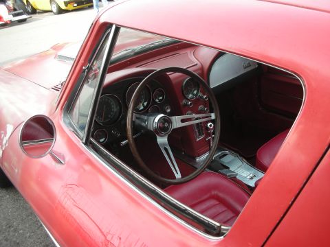 1998 Ford Crown Victoria - View through the side window of a red Corvette cockpit with a wood-rimmed steering wheel, round gauges and red leather seats.