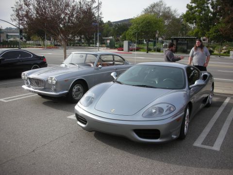 1998 Ford Crown Victoria - silver Ferrari coupe parked alongside a dark vintage coupe in a parking lot, with two people standing in the background.