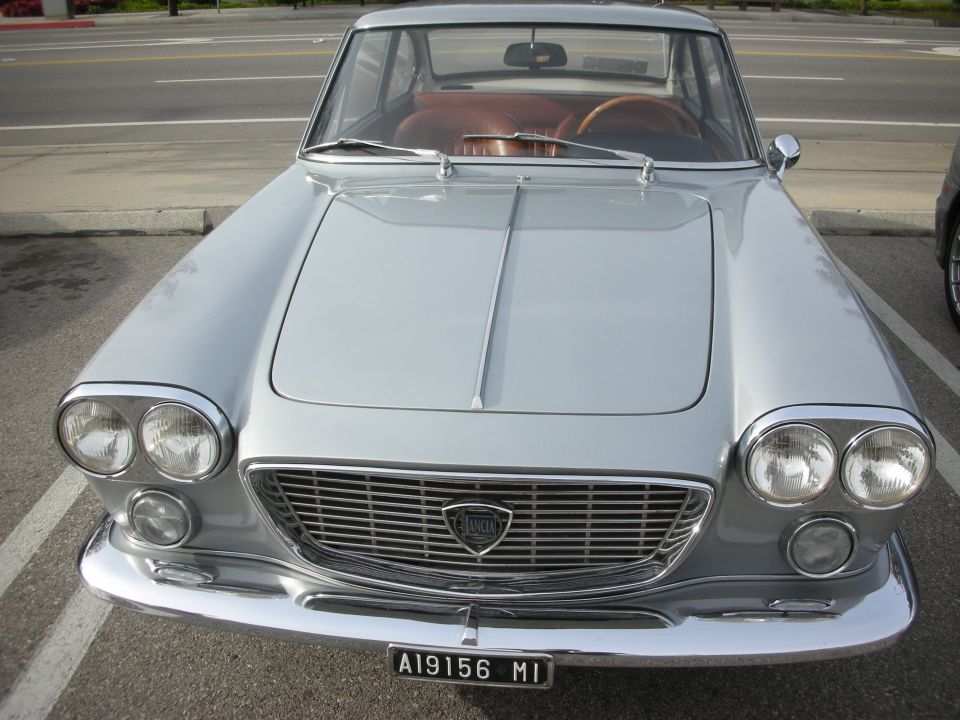 Front of a silver vintage Lancia sedan with quad headlights and chrome grille