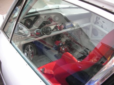 1998 Ford Crown Victoria - View through a window into a stripped race-car interior with red racing bucket seat, roll cage and gauges.