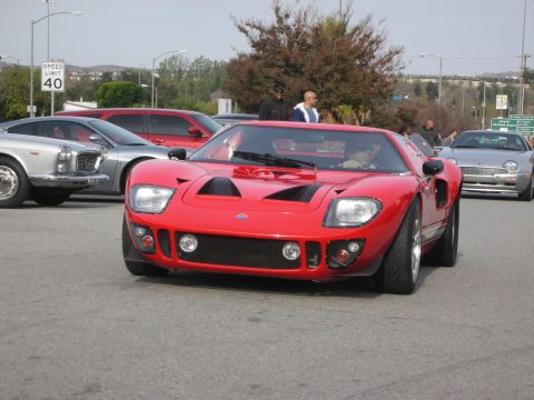 1998 Ford Crown Victoria - red mid-engine GT40-style sports car driving on a street, with onlookers and other cars near a 40 mph speed limit sign.