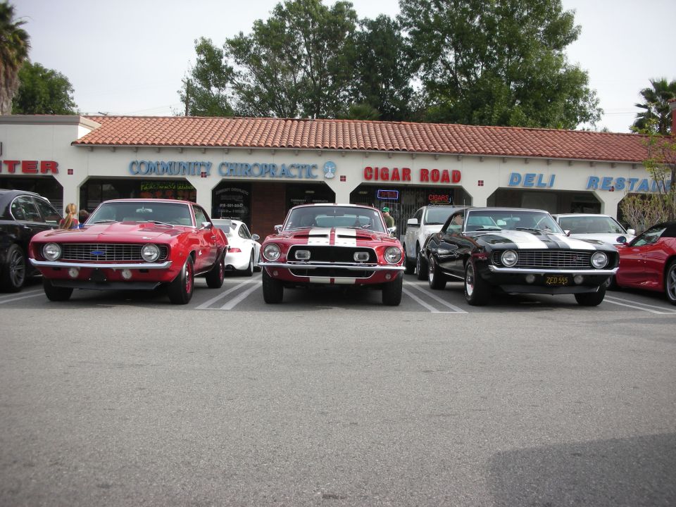 Three classic muscle cars including Camaros and a striped Mustang lined up at show
