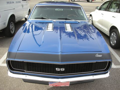 1998 Ford Crown Victoria - Head-on view of a blue first-generation Camaro SS with black grille, cowl-induction hood and an American flag in the front plate area.