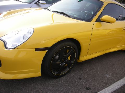 1998 Ford Crown Victoria - Front three-quarter view of a yellow Porsche 911 coupe with black wheels and yellow brake calipers, parked on asphalt.