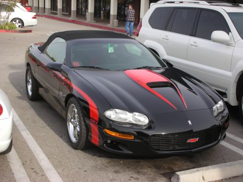 1998 Ford Crown Victoria - black Chevrolet Camaro SS convertible with red stripes and chrome wheels sits in a parking lot among other cars.