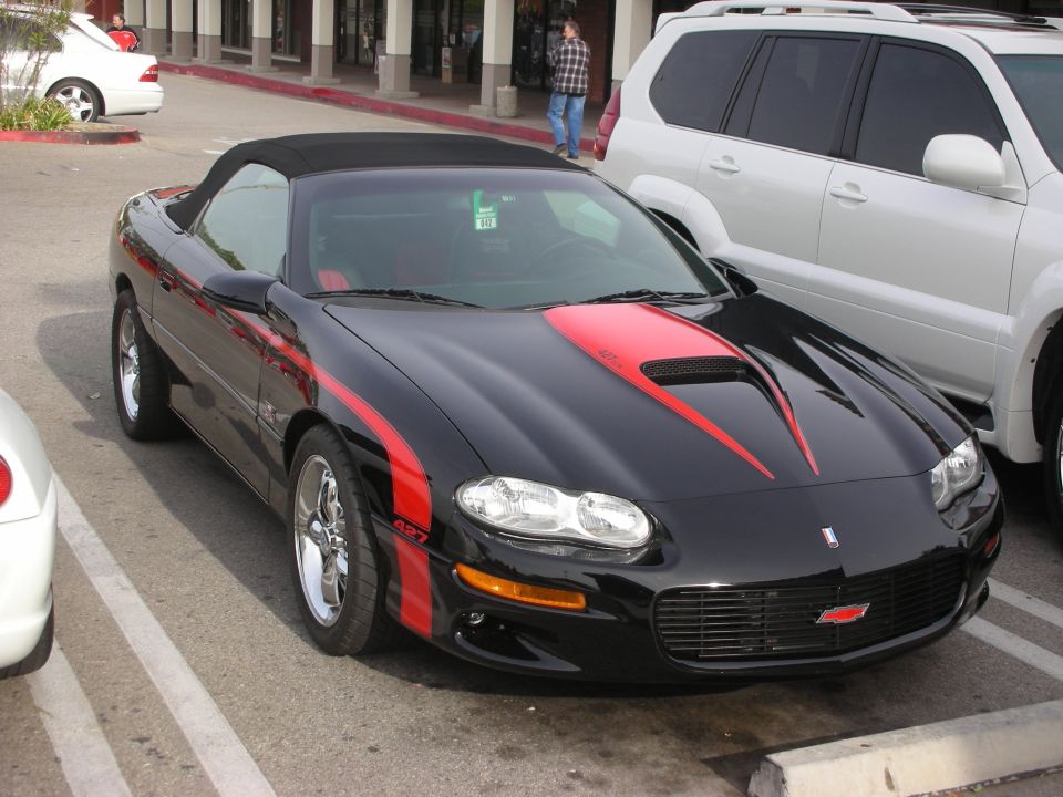 Black Chevrolet Camaro convertible with red SS striping at a parking lot car meet