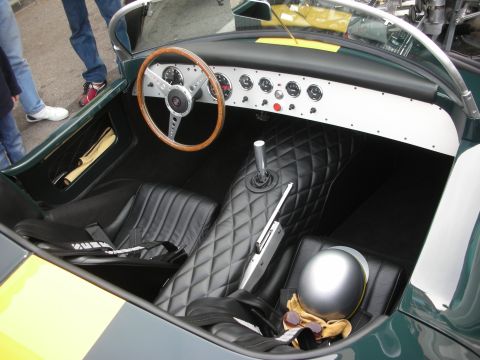 1998 Ford Crown Victoria - Interior of a vintage open roadster showing a wood-rimmed steering wheel, alloy dash, quilted black seats and a silver racing helmet.