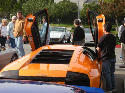 1998 Ford Crown Victoria - orange Lamborghini with its scissor doors raised draws a crowd at a parking-lot car meet.