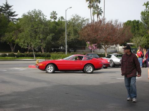 1998 Ford Crown Victoria - red Ferrari Daytona coupe drives across a parking lot as a man in plaid walks past.