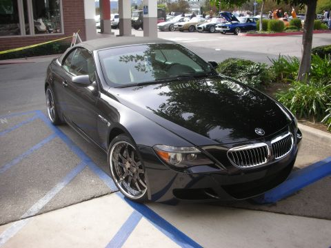 1998 Ford Crown Victoria - black BMW M6 convertible with the top up sits in a marked parking space among show cars.
