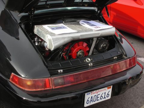 1998 Ford Crown Victoria - Rear engine compartment of a black Porsche 911 showing a red cooling fan and printed papers, with a California plate.