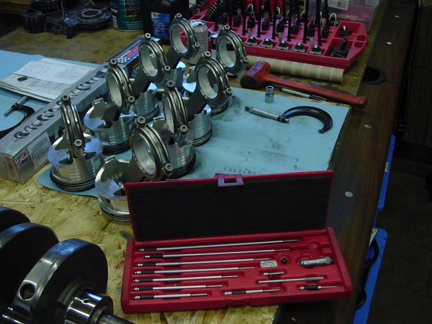 Engine pistons, connecting rods, crankshaft, and measuring tools on a workbench