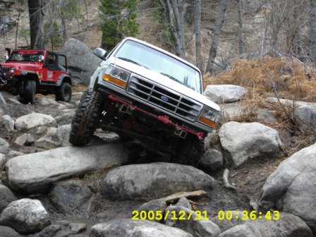 1996 Ford Bronco - White Ford Bronco and red Jeep tackling a challenging rocky off-road course.
