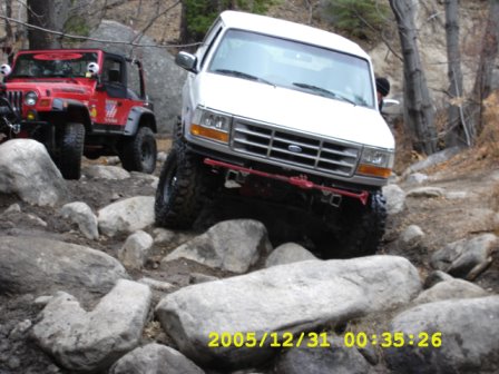 1996 Ford Bronco - A white 1996 Ford Bronco tackles a challenging rocky trail, with a red Jeep visible behind it.