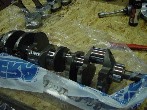 1979 Ford Bronco - Engine components, including a crankshaft and pistons, are laid out on a wooden surface, partially covered in plastic packaging.