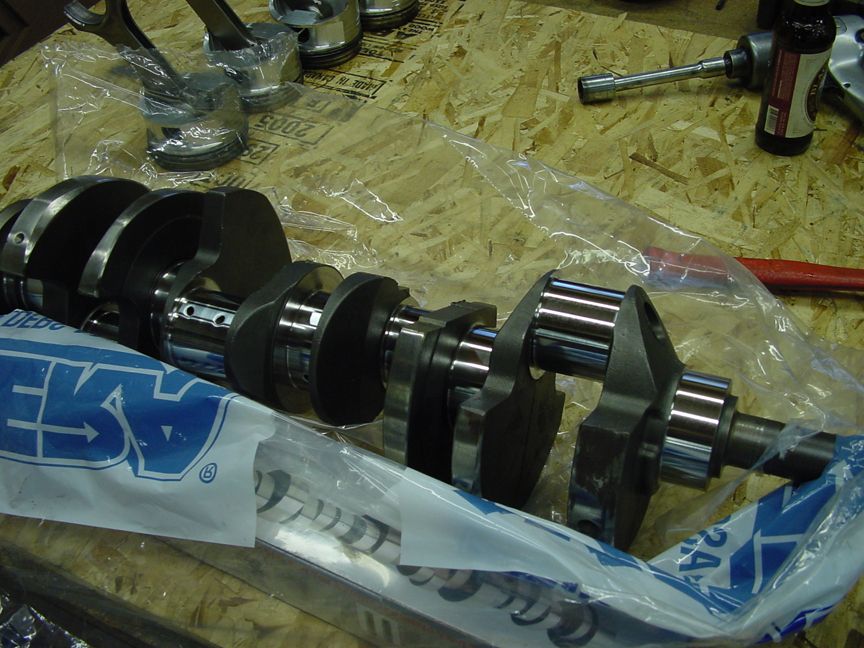 Engine crankshaft and pistons on a wooden surface. Blue packaging with white lettering is visible