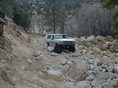 1996 Ford Bronco - A white 1996 Ford Bronco navigates a challenging rocky terrain on an off-road trail.