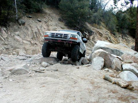 1996 Ford Bronco - A white Ford Bronco is shown off-roading on a challenging rocky terrain.
