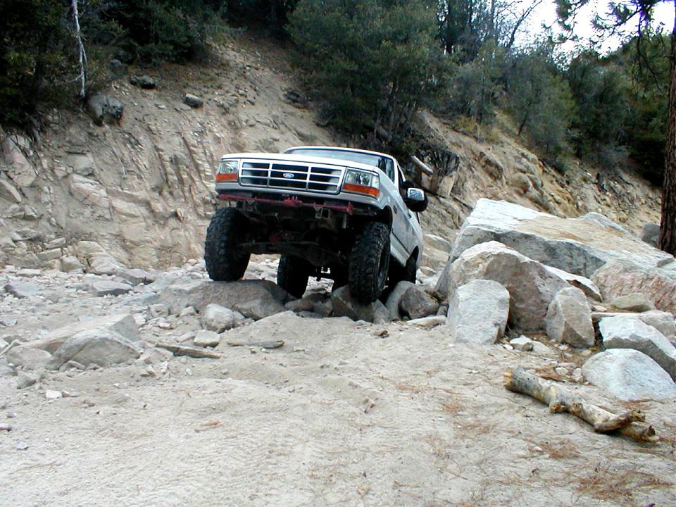 White Ford Bronco navigating a rocky, off-road trail with large boulders