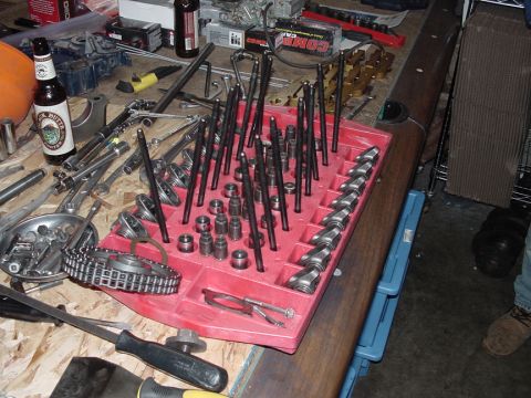 1979 Ford Bronco - A collection of engine parts, tools, and beverages are spread across a workbench.