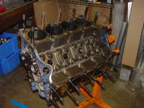 1979 Ford Bronco - Engine block on an orange stand, with bolts protruding from cylinder heads, in a workshop setting.