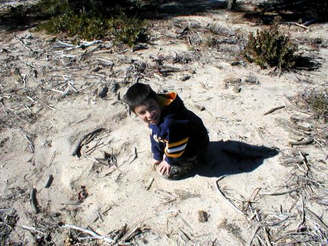 1996 Ford Bronco - Child in sandy terrain with debris and sparse vegetation.