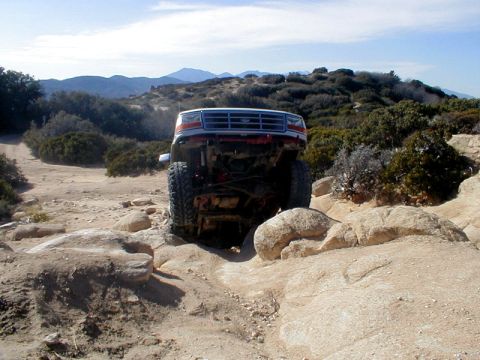 1996 Ford Bronco - White Ford Bronco with red trim is shown from the front, climbing over rocks on a dirt trail.