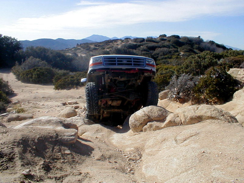 White Ford Bronco with red trim, front view, navigating rocky terrain