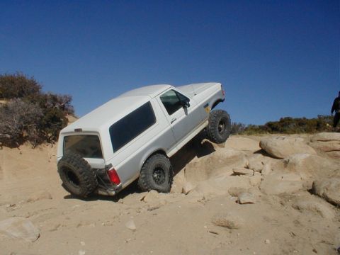 1996 Ford Bronco - A two-tone 1996 Ford Bronco navigates a rocky off-road trail under a clear blue sky.