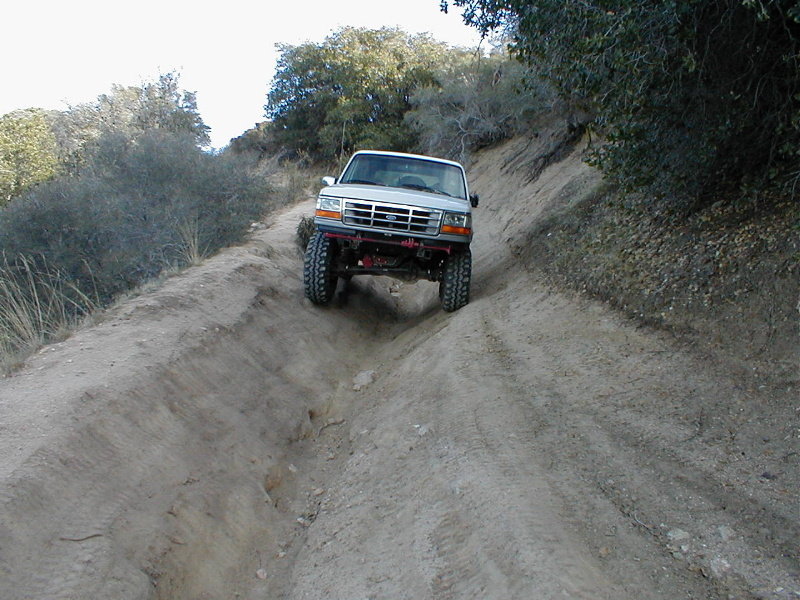 White 1996 Ford Bronco descending a steep dirt trail with large tires