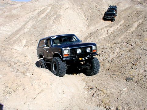 1996 Ford Bronco - Two SUVs navigate a steep, rocky desert trail.