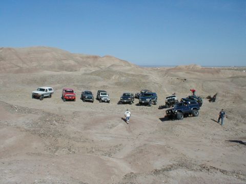 1996 Ford Bronco - Several off-road vehicles are gathered in a dry, hilly terrain under a clear blue sky.