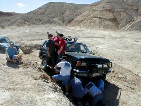1996 Ford Bronco - Several people are working to free a 1996 Ford Bronco stuck in a dirt ditch, with another vehicle nearby.