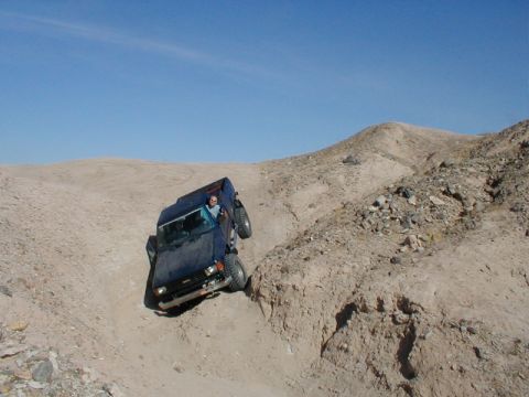 1996 Ford Bronco - A blue SUV navigates a challenging off-road trail under a clear blue sky.