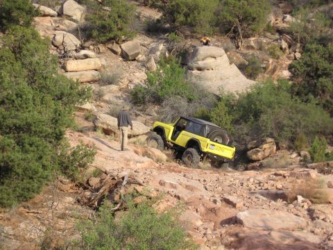 1979 Ford Bronco - A yellow SUV navigates a challenging off-road path with large rocks and sparse vegetation.