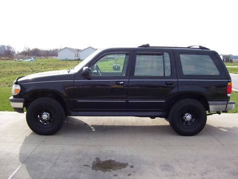 1996 Ford Explorer - This black SUV is parked on a concrete driveway with a grassy field and houses in the background.