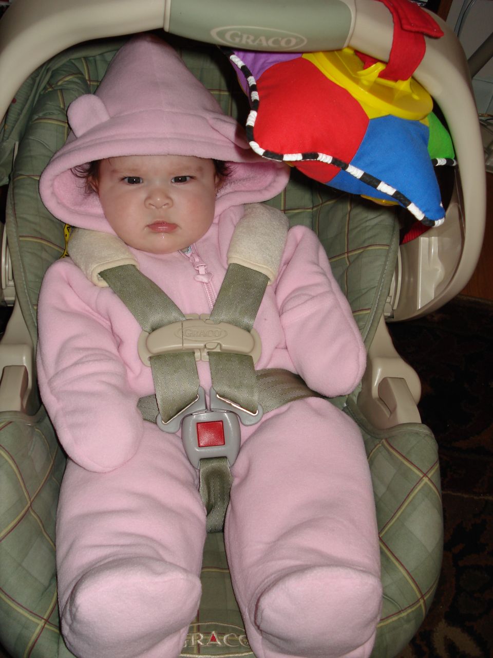 Baby wearing a pink hooded snowsuit sits in a Graco car seat with a colorful toy attached