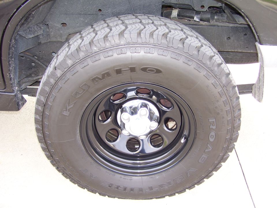 Close-up of a Kumho Venture AT tire on a black rim with chrome lug nut covers