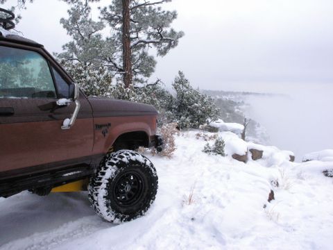 1956 Ford Bronco II - A Ford Bronco sits on a snowy ledge overlooking a misty canyon.