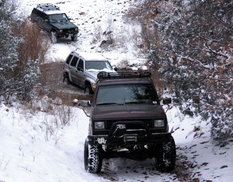 1956 Ford Bronco II - Three SUVs navigate a snowy mountain path during an off-road excursion.