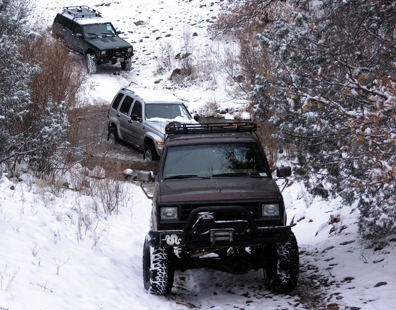 Dark brown Jeep Cherokee XJ with winch and off-road tires driving on a snowy trail