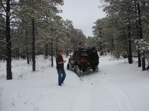 1956 Ford Bronco II - A man stands next to a brown SUV with a spare tire mounted on the rear, driving through a snowy forest.