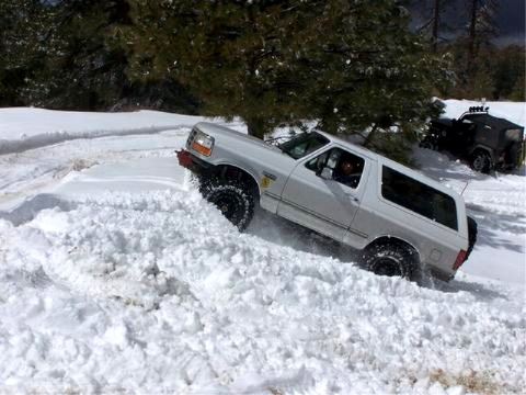 1996 Ford Bronco - White 1996 Ford Bronco navigates a snowy trail with another vehicle visible behind it.